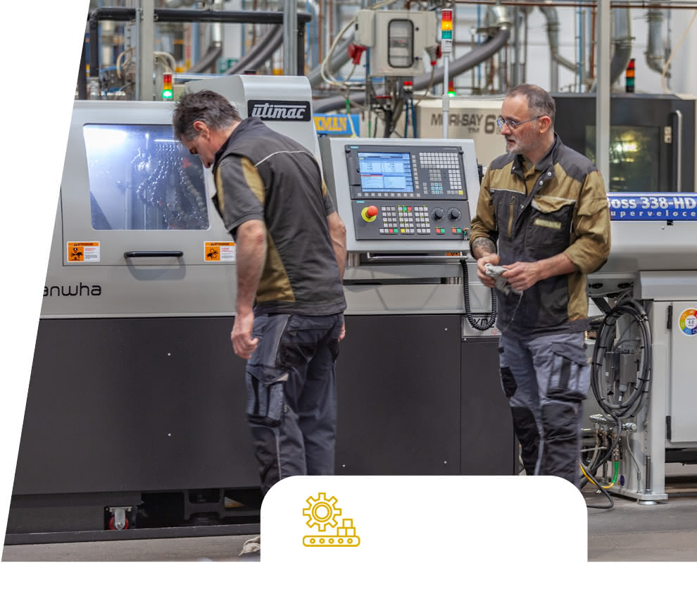 Two Eredi Baitelli operators starting up a CNC lathe, with the production plant visible in the background.
