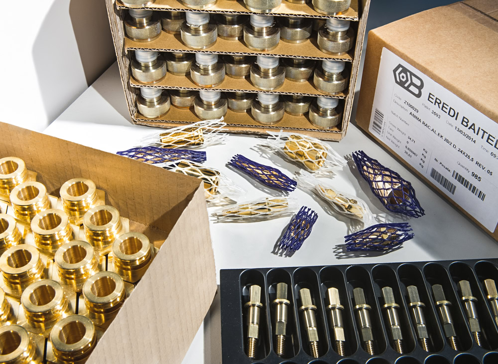 Brass turned parts packed in cardboard dividers, protective nets and thermoformed trays, with an Eredi Baitelli shipping label