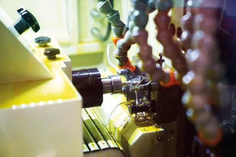 A part being turned on a CNC lathe, with coolant nozzles aimed at the tool