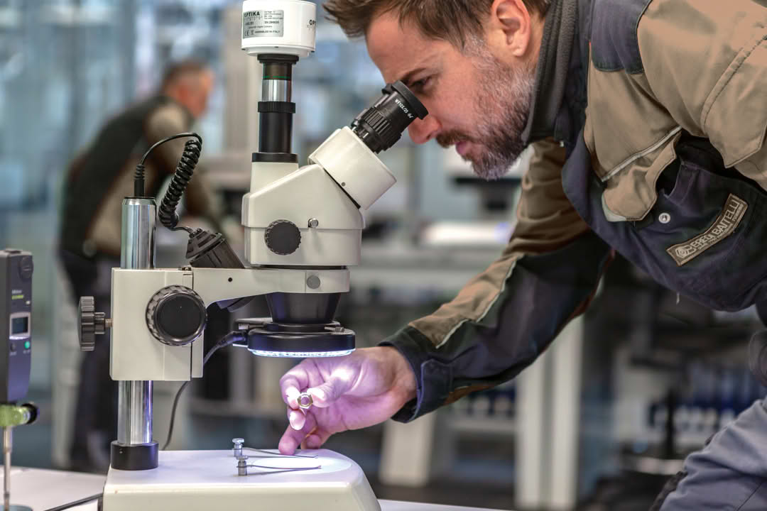Inspector examining a small turned part under a stereo microscope