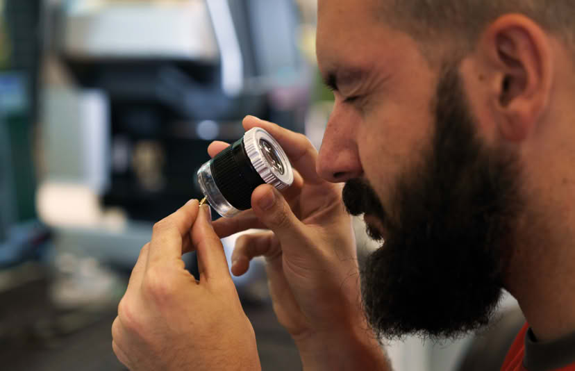 Inspector checking a small turned part with a magnifying loupe